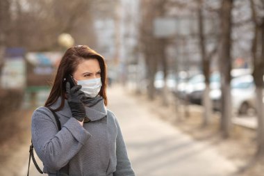 Dışarıda koruyucu tıbbi maske takan bir kadın, yakın çekim. Elinde telefon olan bir kadın. Kişisel bakım kavramını - Görüntü