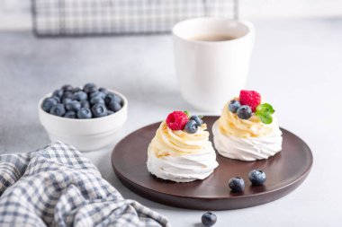 Kahve kupası ve kremalı Pavlova keki ve ahşap tabakta taze böğürtlen. İskandinav tarzı. Yumuşak odak - Resim