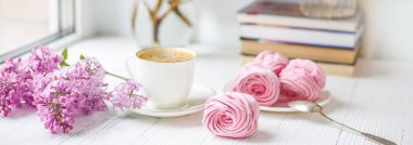 Bir buket leylak, bir fincan kahve, ev yapımı marşmelov ve pencere kenarındaki romantik bahar sabahında yığınla kitap. Seçici odak