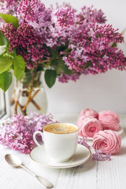 Bir buket leylak, bir fincan kahve, ev yapımı marşmelov ve pencere kenarındaki romantik bahar sabahında yığınla kitap. Seçici odak