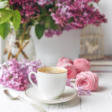 Bir buket leylak, bir fincan kahve, ev yapımı marşmelov ve pencere kenarındaki romantik bahar sabahında yığınla kitap. Seçici odak