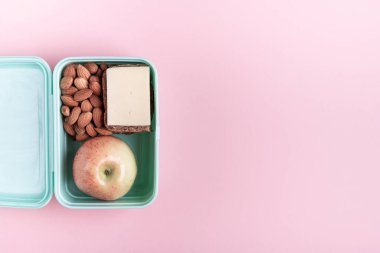 Pembe zemin üzerinde elma, sandviç ve badem olan beslenme çantası metin üst görünümü için kopya alanı ile okula geri dön