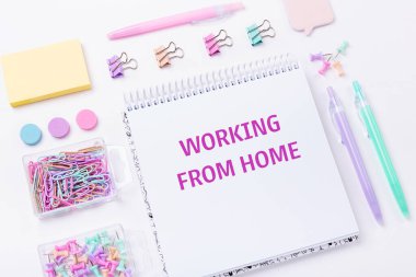Not defteri ve pembe arka planda pastel renkli çalışma aksesuarları olan ev işyeri. Ev konsepti üzerinde çalışıyorum. Üst Görünüm - Resim