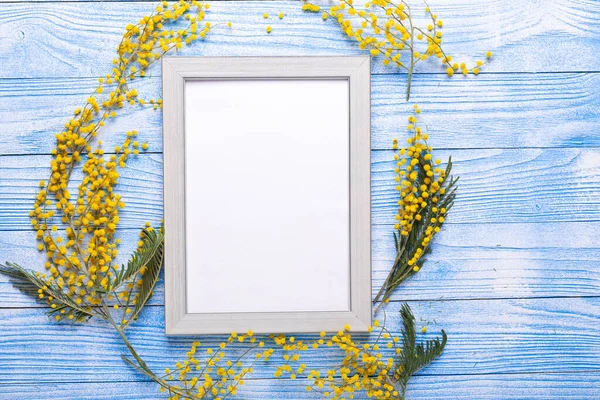 Easter decor with mimosa flowers and frame on blue wooden table. Mockup with a gray frame. Top view. Copy space - Image