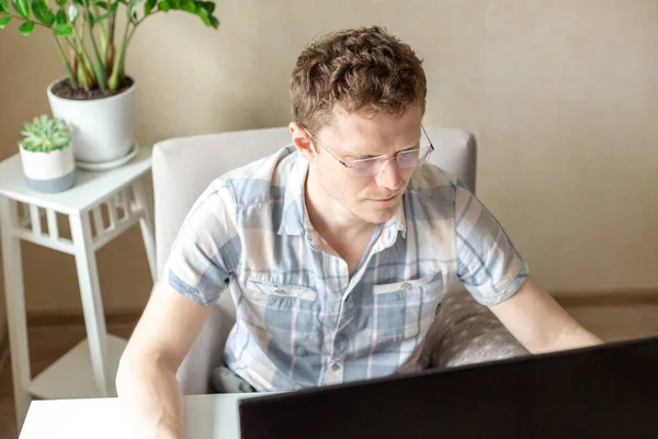 Programmer working from home, remote, home office. A man with glasses looks at the monitor. Remote work concept - Image