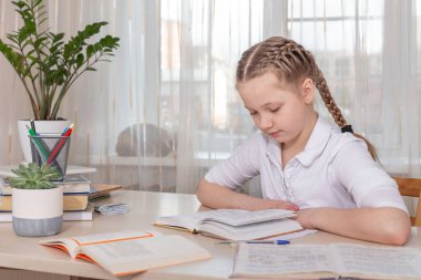 Liseli kız evde ders çalışıyor. Masada kitap okuyan genç bir kız. Uzaktan eğitim, evde eğitim. Kişisel izolasyon kavramı - Resim