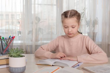 Liseli kız evde ders çalışıyor. Masada kitap okuyan genç bir kız. Uzaktan eğitim, evde eğitim. Kişisel izolasyon kavramı - Resim