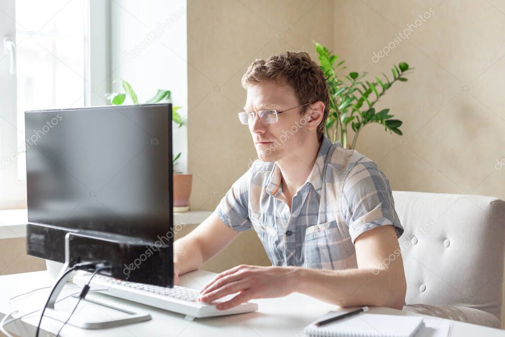 Programmer working from home, remote, home office. A man with glasses looks at the monitor. Remote work concept - Image