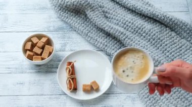Kadın eli bardağı masaya kahve ile koyar. Kahve fincanı, kazak, tarçın, esmer şeker. Sıcak sonbahar kompozisyonu. Hygge konsepti. 4K görüntü