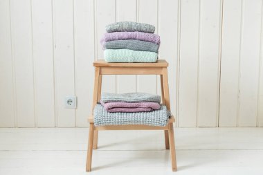 Ahşap bir merdivende bir yığın rahat örgü kıyafet. İskandinav tarzı. Beyaz ahşap duvar