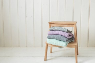 Ahşap bir merdivende örülmüş bir kazak yığını. İskandinav tarzı. Beyaz ahşap duvar