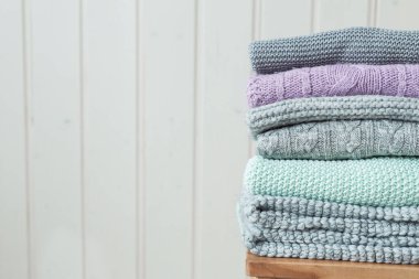 Ahşap bir merdivende örülmüş bir kazak yığını. İskandinav tarzı. Beyaz ahşap duvar