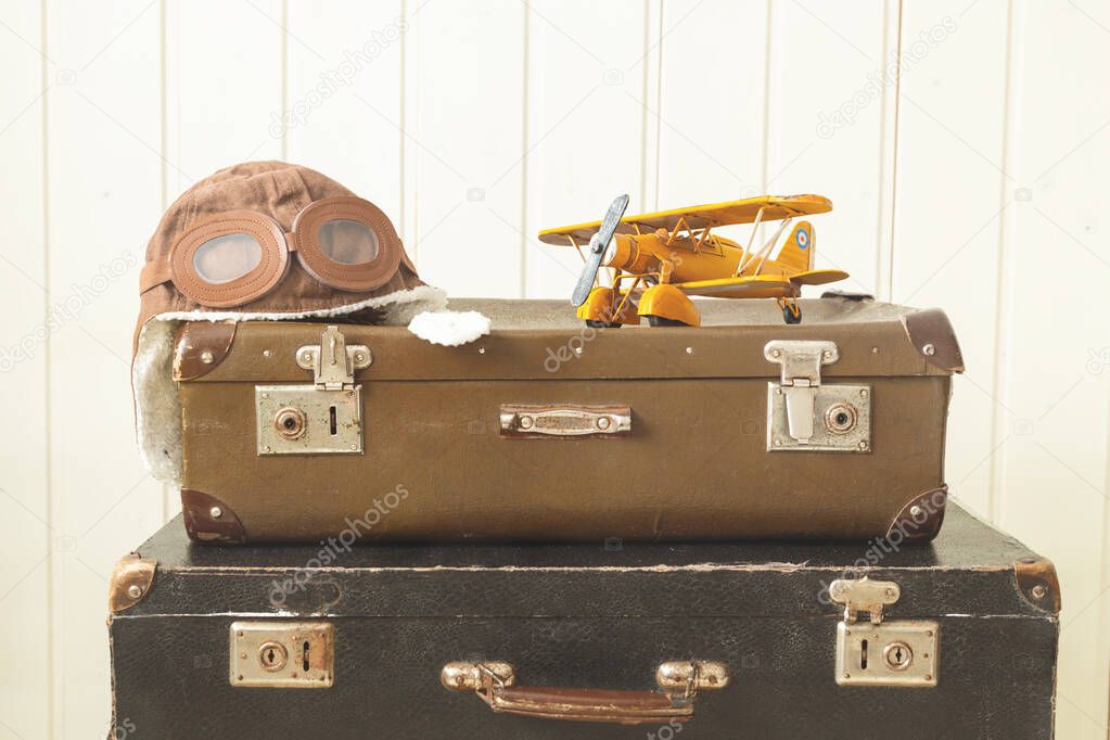 Helmet pilot and toy yellow metal plane Two old retro suitcases White wooden background Vintage tinting Copy space