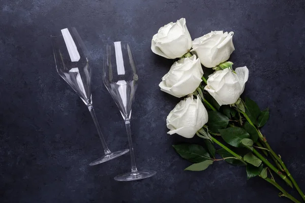 White rose flowers bouquet, champagne glasses on black stone background Romantic greeting card Copy space Top view