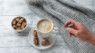 Kadın eli bir kahve fincanı alır. Kahve fincanı, kazak, tarçın, esmer şeker. Sıcak sonbahar kompozisyonu. Hygge konsepti. 4K görüntü