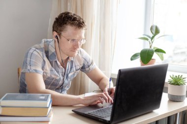 Evden, uzaktan, ev ofisinden çalışan kulaklıklı programcı. Gözlüklü bir adam monitöre bakıyor. Uzak çalışma konsepti - Resim