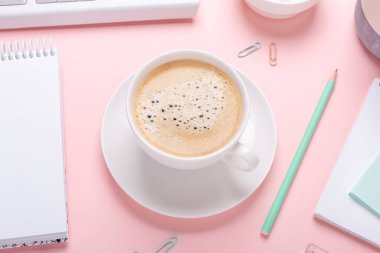 Pembe arka planda bir fincan kahve ve pastel renkli kırtasiye aksesuarları olan kadın işyeri. Üst Görünüm - Resim