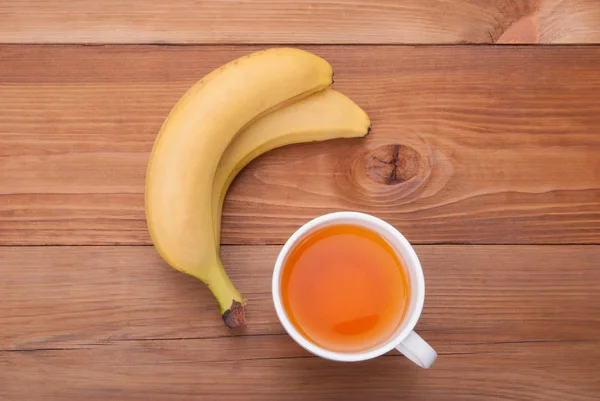 A cup of hot tea and bananas on a wooden background. — Stock Photo, Image