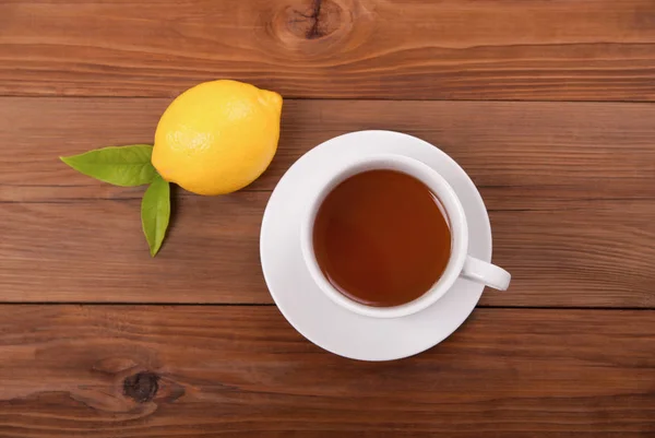 Чашка чая и лимона с листьями на деревянном фоне — стоковое фото