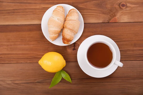 Taza de té con limón y croissants sobre fondo de madera . — Foto de Stock