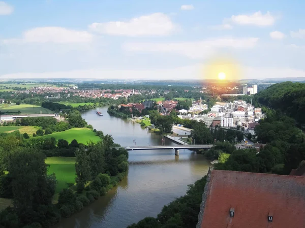 A beautiful sunset on the horizon is seen from the tall, old tower in Bad Wimpfen, and a cargo ship sails on the curved river Neckar