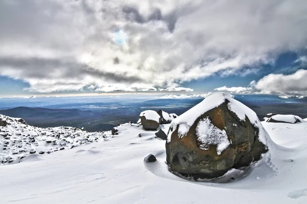 El sol se asoma a través de las nubes sobre un campo de nieve rocoso en las laderas del monte. Ruapehu en Nueva Zelanda —  Fotos de Stock