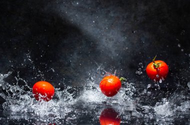 Gri arkaplanda su damlalarında uçan kırmızı domatesler