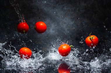 Gri arkaplanda su damlalarında uçan kırmızı domatesler
