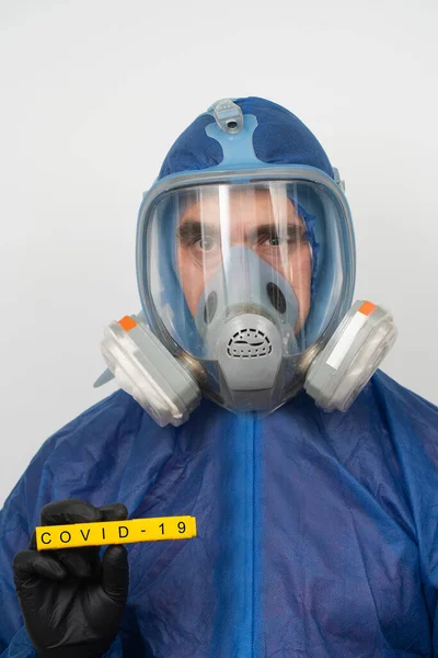 a man in a protective suit and mask holds a sign that reads covid 19