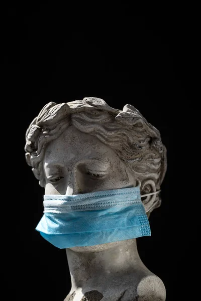 antique statue head in a protective mask on black background