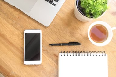 Ofis Resepsiyon ahşap masaları ile akıllı telefon, fincan çay, dizüstü bilgisayar, kalem, bitki ve defter. Üstten Görünüm kopya alanı ile. Evde çalışma ve office kavramı.