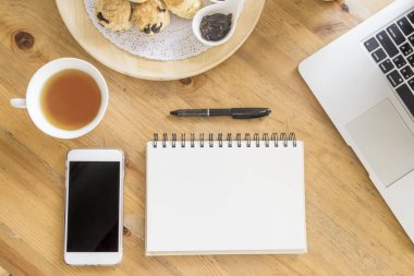 Ofis Resepsiyon ahşap masaları ile akıllı telefon, fincan çay, dizüstü bilgisayar, kalem, bitki ve defter. Üstten Görünüm kopya alanı ile. Evde çalışma ve office kavramı.