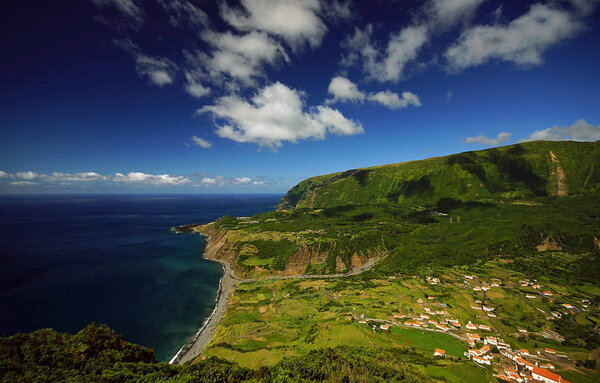 Incredible view of small village on ocean coast on Flores island, Azores. Bright green ladscape and blue sky with clouds           