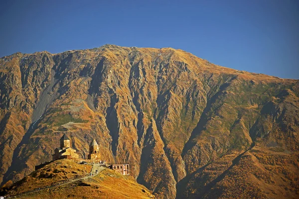 Kazbegi Dağı 'nın altındaki Gergeti Trinity Kilisesi' nin güzel manzarası kahverengi dağlar ve mavi gökyüzü, Kafkasya, Gürcistan