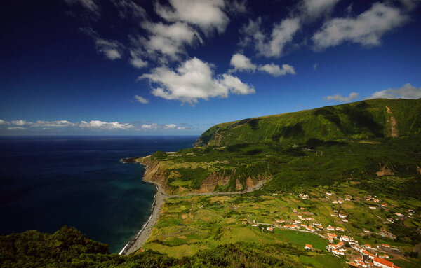 Incredible view from top of small village on ocean coast. Bright green ladscape, blue sky with clouds