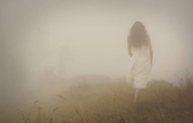 Woman in long white dress going in foggy mist. Blur discernible outline of figure. View from behind. Mistery landscape clipart
