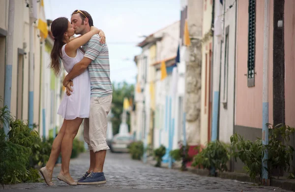Romantic photo of young kissing couple standing on street in small cozy town. Background of small colorful houses