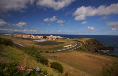 Sunny view of takeoff runway of small airport on rock shore. Background of bright blue sky and small cozy village