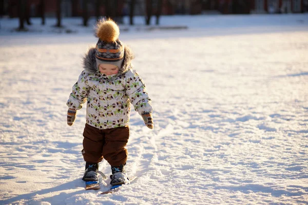 Солнечный зимний портрет улыбающегося мальчика-лыжника в яркой одежде и шляпе с пумой, стоящего на лыжах в снежном парке — стоковое фото