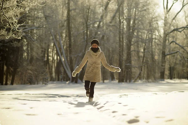 Портрет молодой женщины в белом халате, гуляющей в солнечном снежном лесу на рассвете зимой, морозной солнечной зимой — стоковое фото