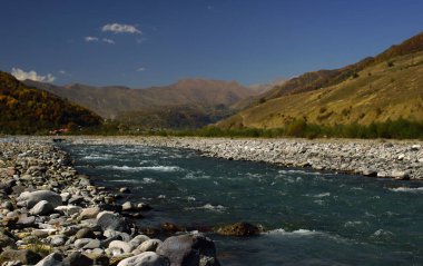 Dağlar, Gürcistan Askeri Yolu, Gürcistan çevresindeki yeşil vadide mavi su ve kaya bankaları ile çalkantılı bir nehir.