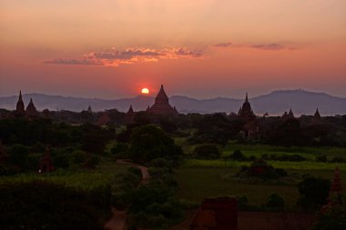 Bagan tapınakları ve vadideki pagodalar üzerinde güzel bir günbatımı, Burma Myanmar. Güneş ufukta ve dağlarda batıyor.