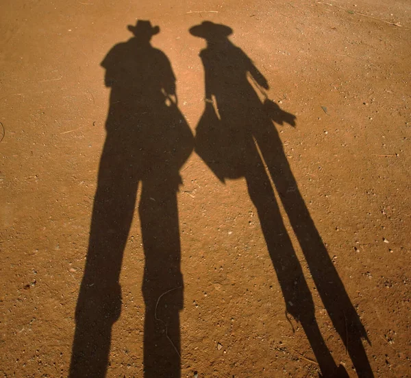 Ombre noire de couple sur sable jaune, silhouette de jeune femme voyageuse et homme en chapeaux avec appareil photo et sacs — Photo