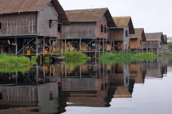 Bamboo houses on piles standing in water in township on Inle Lake in Burma, mirror reflection of houses in still water