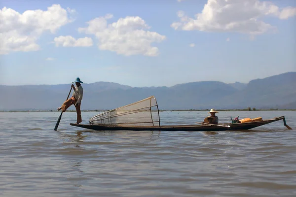 Nyaung Shwe en Inle Lake, Birmania - 4 de diciembre de 2012. Hombre birmano remando un barco con una pierna. Red de pesca de cono en barco — Foto de Stock