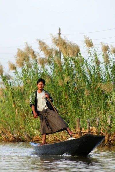 Nyaung Shwe en Inle Lake, Birmania - 4 de diciembre de 2012. Joven hombre birmano remando un barco con una pierna en el jardín flotante — Foto de Stock