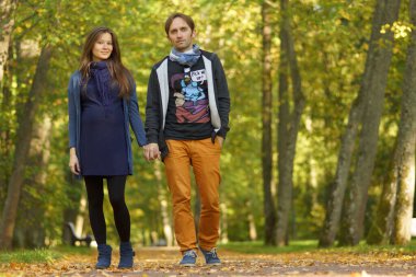 Genç, çekici, hamile bir kadın ve mutlu bir adam, güneşli yeşil parkta yürüyor. 9 aylık hamilelik