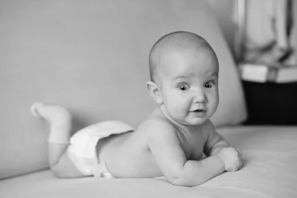 Чорно-білий портрет маленької новонародженої дитини, що лежить на животі. Маленька дитина з великими очима в серветці і шкарпетках, крупним планом — стокове фото