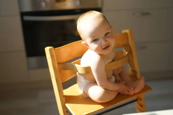 Маленька усміхнена дитина сидить у дерев'яному високому стільці на сонці на кухні і дивиться вгору, вид зверху. Сонячна фотографія — стокове фото