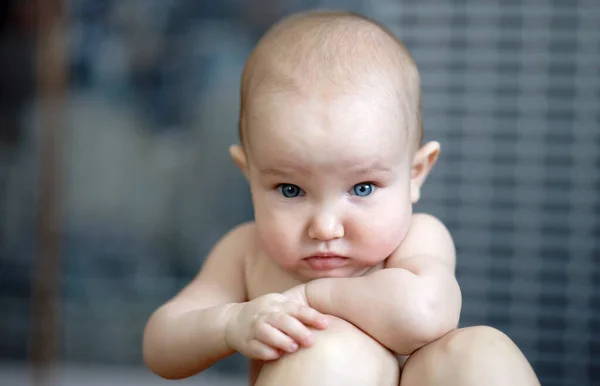 Porträt eines kleinen nachdenklichen Babys mit großen blauen Augen. Nettes Kind mit kurzen Haaren, ohne Hemd. Grauer Hintergrund — Stockfoto